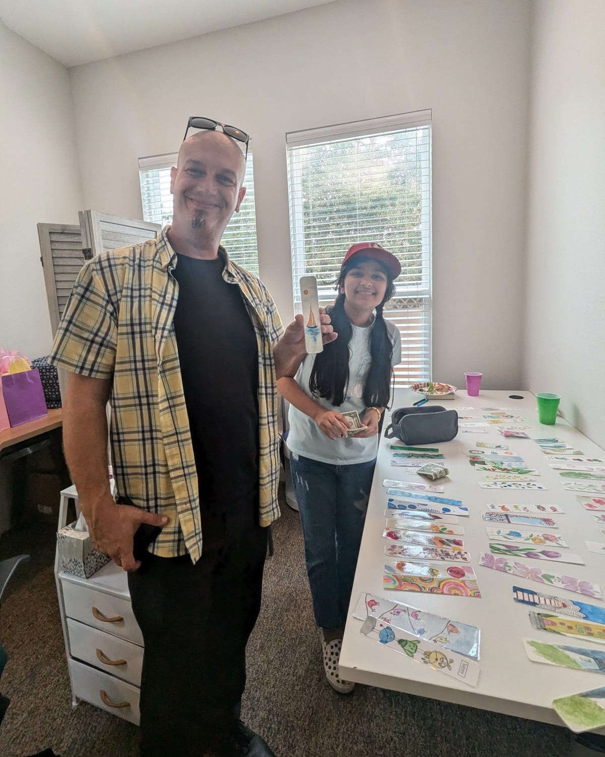 A customer holding up the bookmark he just bought from Viti, who holds his payment