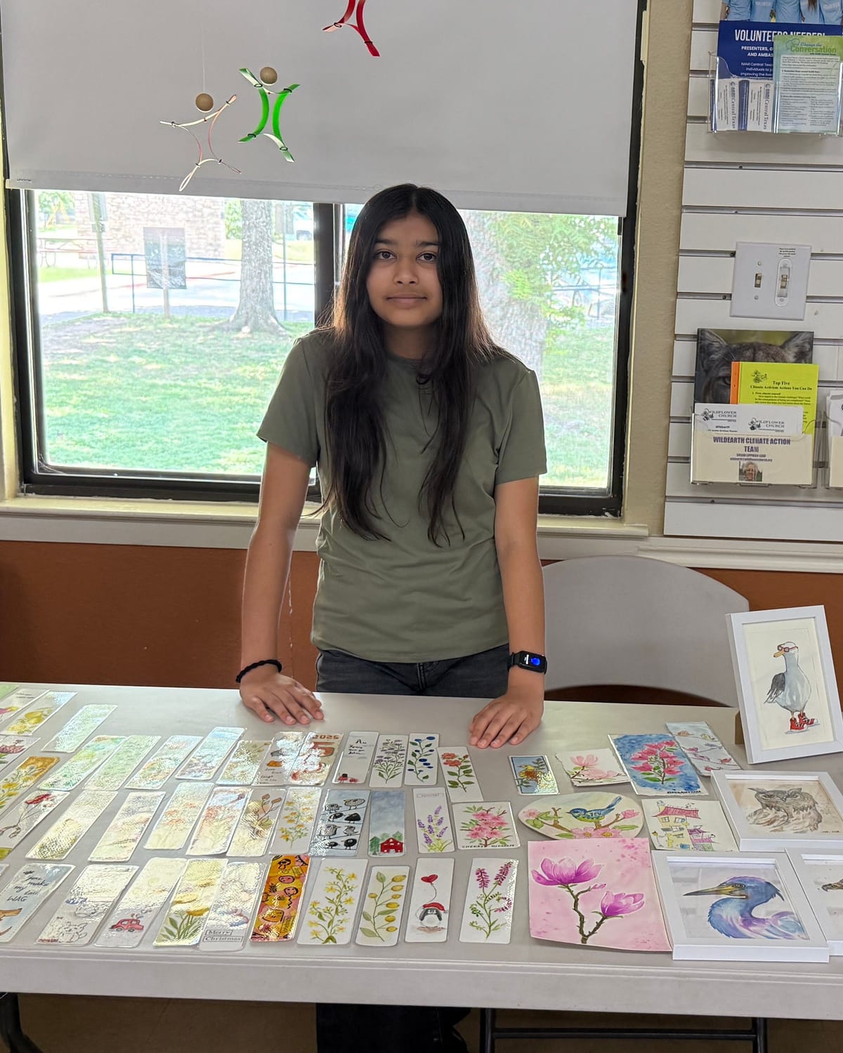 Viti standing behind her table of handmade bookmarks and framed bird paintings