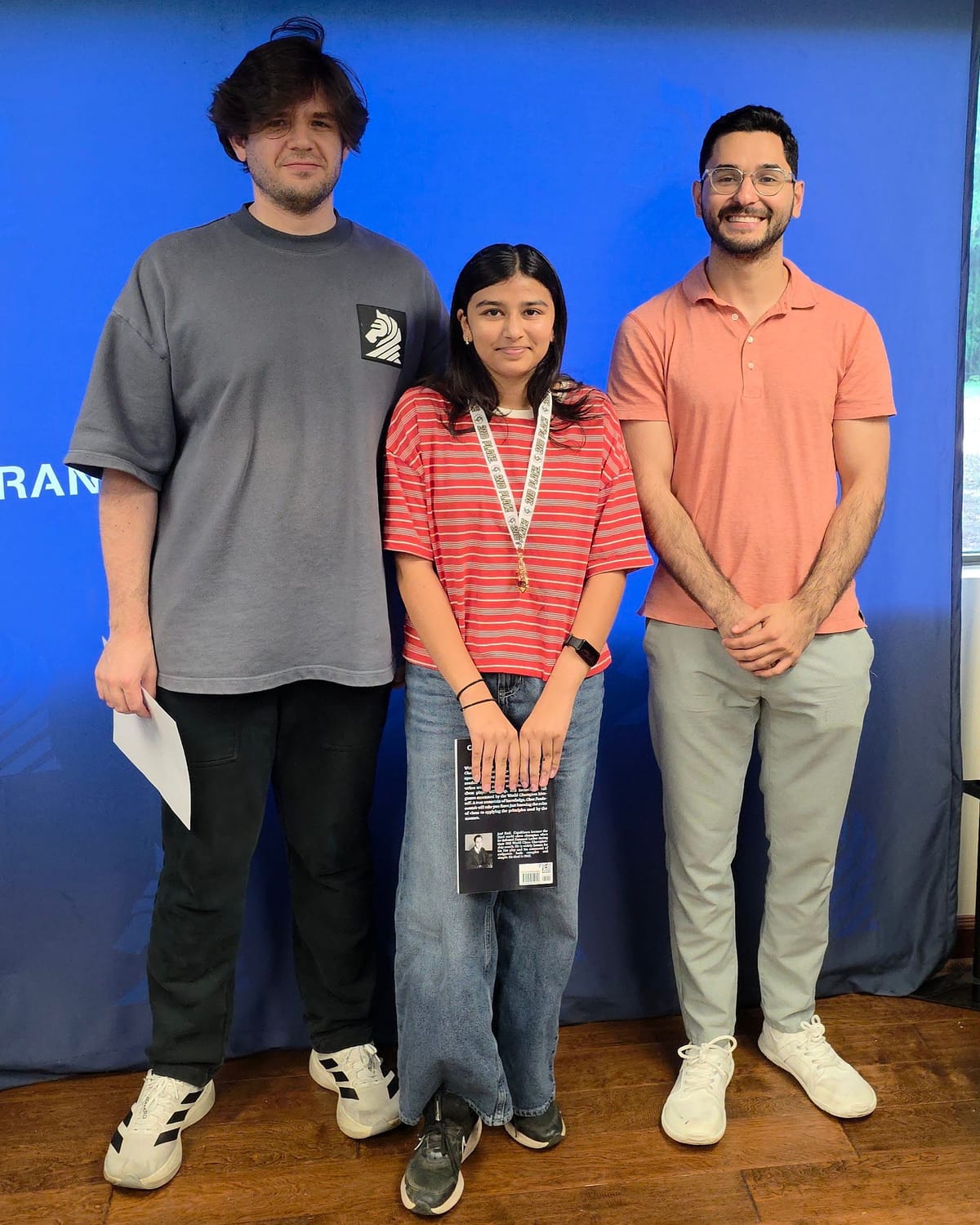 Viti wearing her medal and holding a prize book, standing with two adults after the tournament