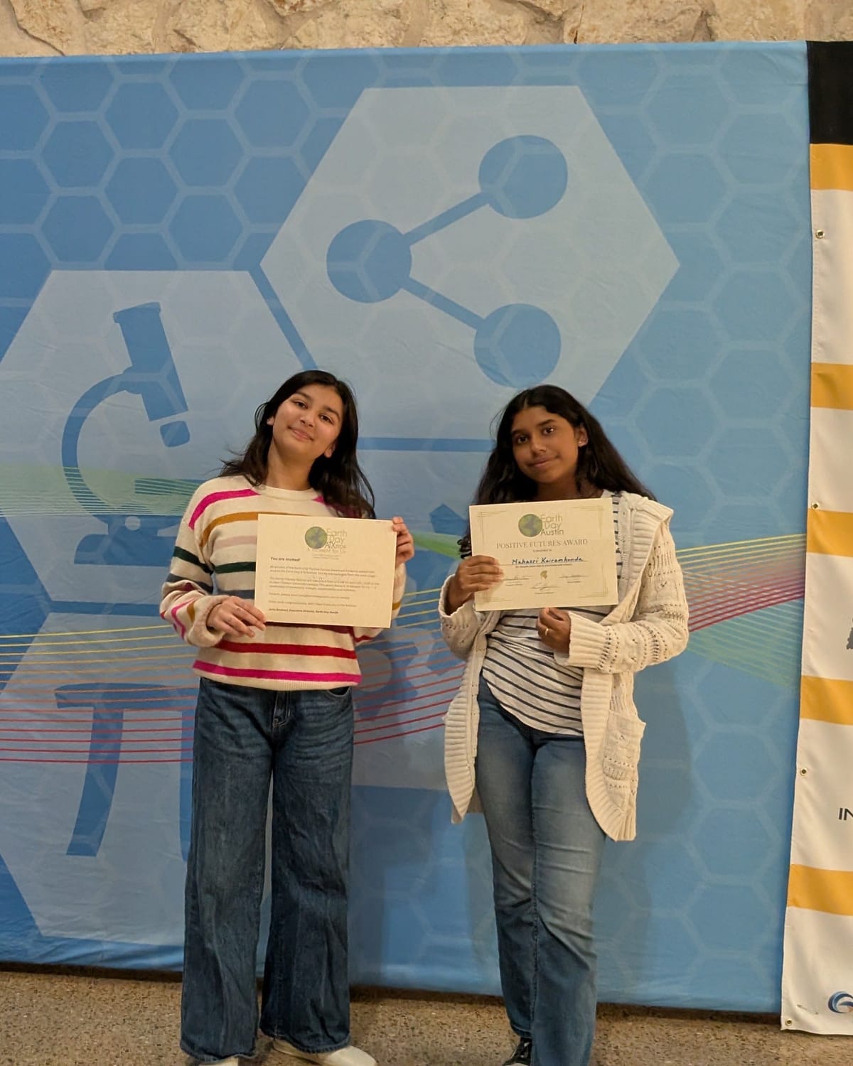 Viti and her teammate holding their award certificates in front of the GARSEF banner