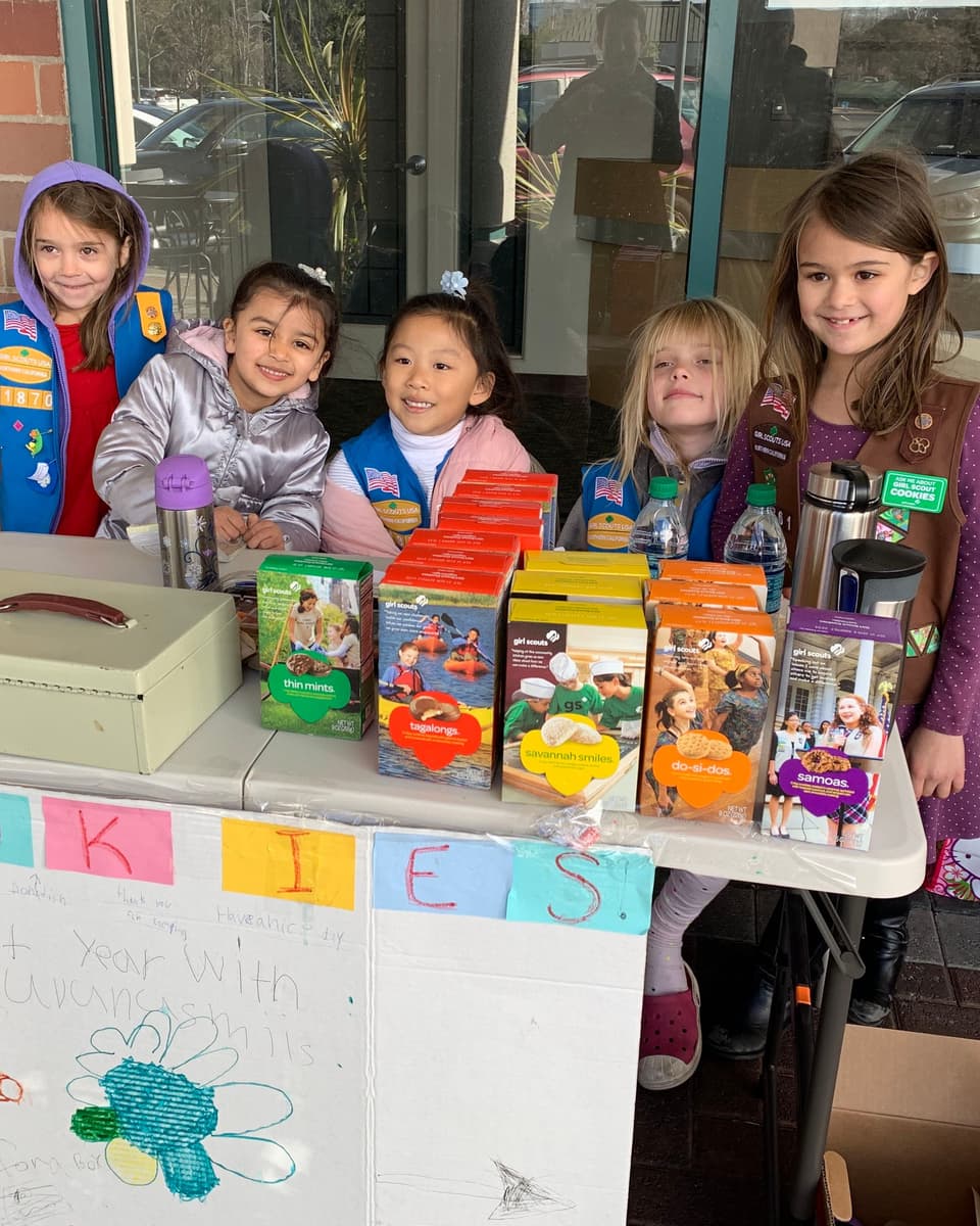 Viti and fellow Girl Scouts smiling behind their cookie booth table