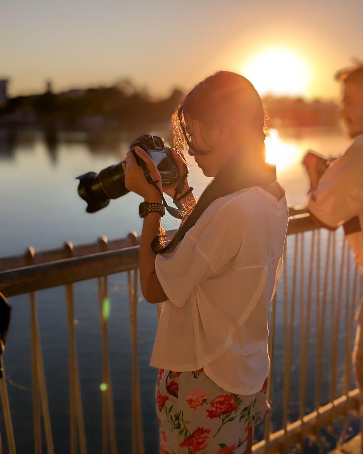 Viti framing a shot with her camera by the water at sunset