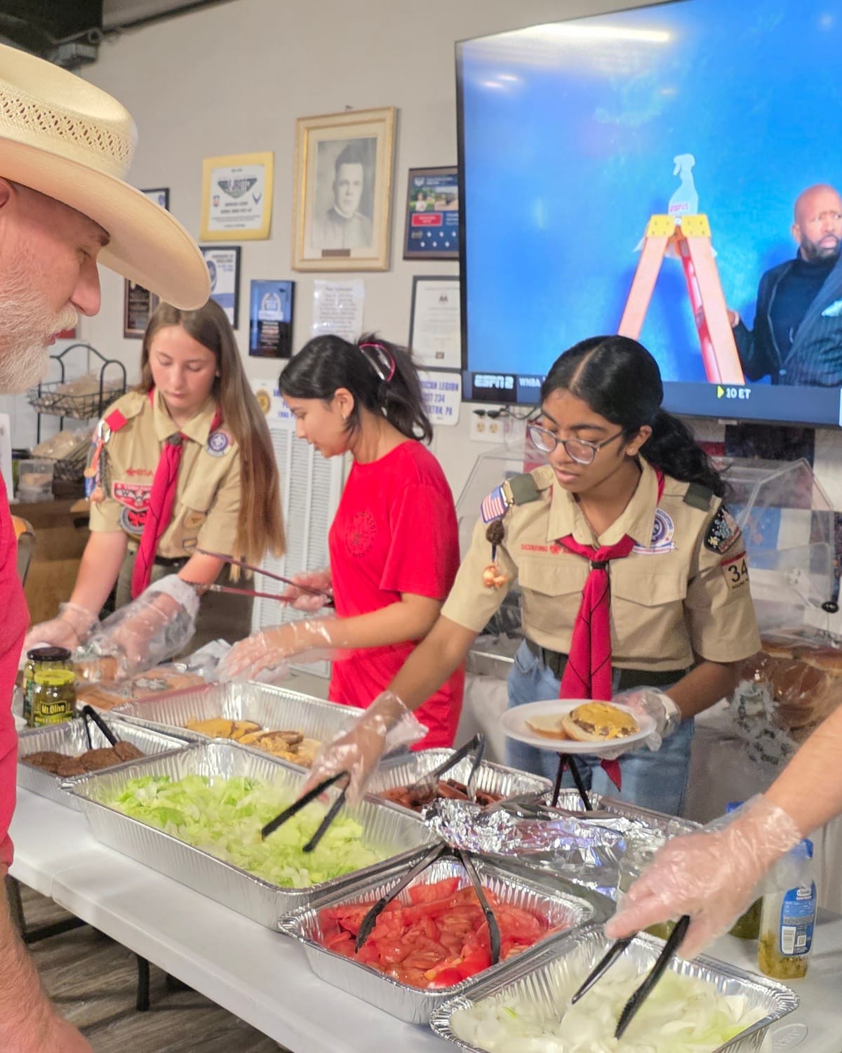 Viti and fellow scouts in gloves serving food along a buffet line for veterans